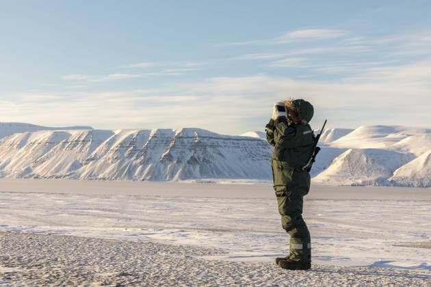 Ein Mann mit Gewehr und Fernglas blickt auf den Horizont in der arktischen Landschaft in Billefjorden, Spitzbergen in Norwegen. Eisbären besuchen dieses Gebiet, und das Gewehr ist im Falle eines Angriffs notwendig, auch wenn es sehr selten ist Man with a rifle and binoculars looks out on the horizon in arctic landscape in Billefjorden, Svalbard in Norway. Polar bears visit this area, and the rifle is necessary in case of an attack, even if it is very rare Copyright: imageBROKER LillianxTveit ibxiqx15340840.jpg