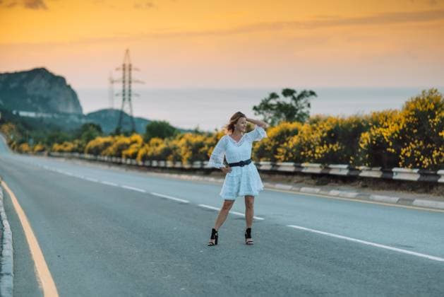 A woman in a white dress is standing on a road, looking at the camera A woman in a white dress is standing on a road, looking at the camera. The scene is set against a backdrop of a beautiful sunset, with the sky turning orange and pink. The woman is enjoying the moment, model released, , 62026546.jpg RECORD DATE NOT STATED