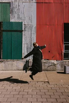 Black hispanic woman in coat jumps with joy in front of building Québec City, Quebec, Canada CR_WVNP251106-1842445-01 ,model released, Symbolfoto