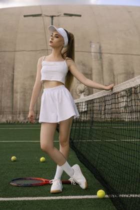 Ein junger Athlet in einem weißen Tennisoutfit steht am Netz und zeigt während der Goldenen Stunde auf einem grünen Platz, umgeben von Tennisbällen, Selbstvertrauen A young athlete in a white tennis outfit stands by the net, showcasing confidence on a green court surrounded by tennis balls during golden hour Copyright: imageBROKER AndreyxGuryanov ibxgur15622593.jpg ,model released, Symbolfoto ,property released