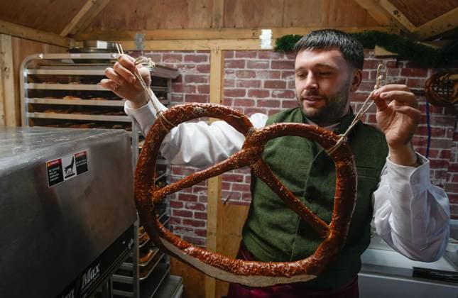 (251115) -- VANCOUVER, Nov. 15, 2025 -- A vendor shows a large pretzel in a wooden hut at the Vancouver Christmas Market in Vancouver, British Columbia, Canada, Nov. 14, 2025. The annual festive event features more than 110 wooden huts offering various handicrafts, traditional European food, drink, and souvenirs, along with live performances. This year s market opened here on Thursday and will run until Dec. 24. (Photo by Xinhua) CANADA-VANCOUVER-CHRISTMAS MARKET LiangxSen
