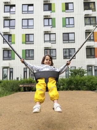 Kleines Mädchen in gelben Hosen, das auf dem Spielplatz mit modernem Wohnhaus im Hintergrund schwingt, Konzept von Freude und Kindheitsaktivität, Kindheitskonzept Little girl in yellow pants swinging in playground with modern apartment building in background, concept of joy and childhood activity, childhood concept Copyright: imageBROKER EvgeniiaxGordeeva ibxiqx15556012.jpg ,model released, Symbolfoto ,property released