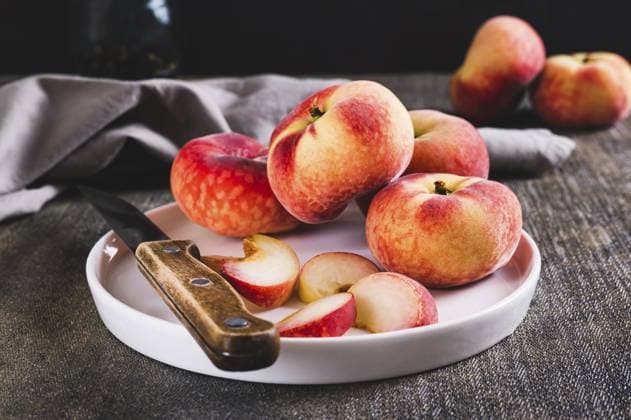 Ganze und geschnittene Pfirsiche und ein Messer werden auf einen Teller auf dem Tisch gelegt Whole and sliced peaches and a knife are placed on a plate on the table Copyright: imageBROKER ElenaxRui ibxiqx15559283.jpg