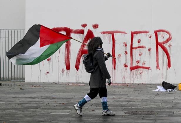 Activists protest German arms policy by leaving red prints on Chancellery wall BERLIN, GERMANY - NOVEMBER 18: A woman holding a Palestinian flag walks in front of a wall with the word Taeter (Perpetrator) written on it, as the Peacefully Against Genocide group stages a protest in front of the chancellery building in Berlin, Germany on November 18, 2025. Halil Sagirkaya Anadolu Berlin Germany. Editorial use only. Please get in touch for any other usage.  Copyright: x2025xAnadoluxHalilxSagirkayax