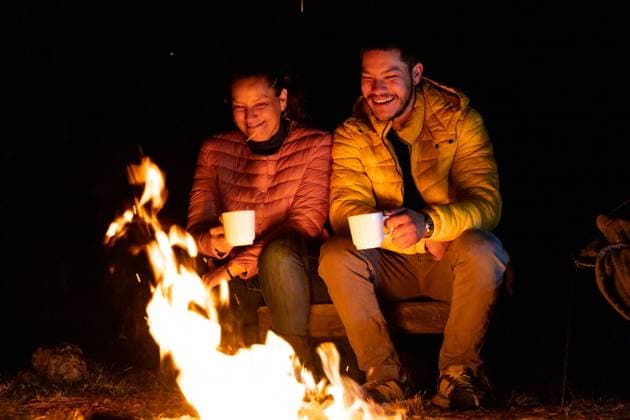A man and a woman enjoy a cozy campfire under a starlit sky, sipping warm drinks from white mugs in the forest. The orange flames provide warmth and light in the tranquil night. Model Released EduardoGavira_ID26515_765388_029 Copyright: xx