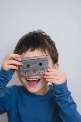 Smiling child holding audio cassette playfully in blue shirt indoors model released, Symbolfoto property released, ANAF05256