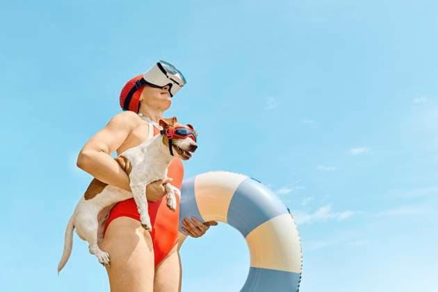 Woman in red swimsuit with virtual reality glasses holding a Jack Russell Terrier and a swimming ring outdoors model released, Symbolfoto property released, CATF00646