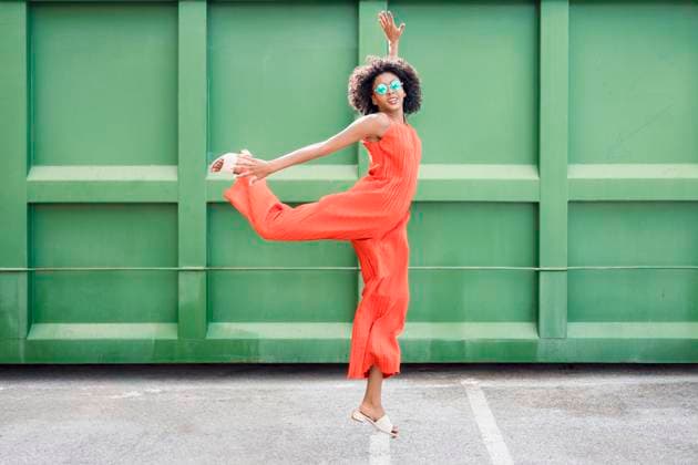 Fashionable woman with afro hairstyle jumping joyfully by green wall model released, Symbolfoto, JSMF03476