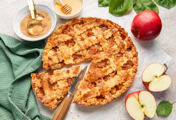 Freshly baked apple pie with a slice cut out, surrounded by apples and baking ingredients Model Released OlenaRudo_ID32506_1107596_036 Copyright: xOlenaxRudox