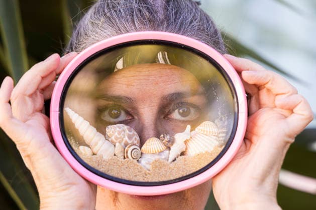 Creative summer concept portrait of a beautiful woman wearing pink diving goggles filled with beach sand, seashells, and sea snails. Symbol of summer vacation, beach lifestyle, travel, and holiday mood Model Released SylviePm_ID32199_1096437_001 Copyright: xx RECORD DATE NOT STATED