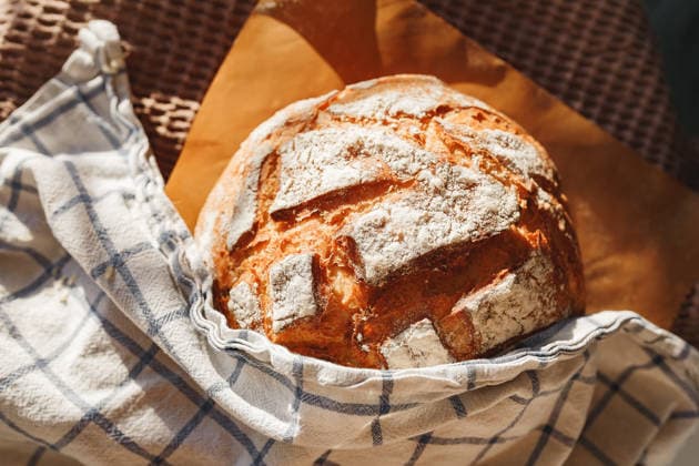 Freshly baked rustic bread wrapped in a cloth A warm, rustic loaf of bread with a golden crust is wrapped in a checkered cloth, emanating a comforting aroma. Sunlight highlights the artisanal texture of the bread. Model Released Aveamig_ID32432_1105238_006 Copyright: xx RECORD DATE NOT STATED