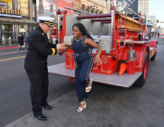 Eniola Taiwo and LAFD Chief Jaime E. Moore arrive for an unveiling ceremony honoring the Los Angeles Fire Department with an Award of Excellence star adjacent to the Hollywood Walk of Fame in Los Angeles on Tuesday, December 2, 2025. Taiwo, 14, wrote a letter to the Hollywood Chamber of Commerce suggesting that firefighters who battled the deadly January fires were worthy of a star on the Hollywood Walk of Fame. The letter precipitated the tribute.  LAP2025121203 JIMxRUYMEN