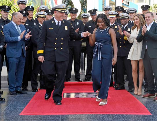 Eniola Taiwo (R) and LAFD Chief Jaime E. Moore participate in an unveiling ceremony honoring the Los Angeles Fire Department with an Award of Excellence star adjacent to the Hollywood Walk of Fame in Los Angeles on Tuesday, December 2, 2025. Taiwo, 14, wrote a letter to the Hollywood Chamber of Commerce suggesting that firefighters who battled the deadly January fires were worthy of a star on the Hollywood Walk of Fame. The letter precipitated the tribute.  LAP2025121206 JIMxRUYMEN