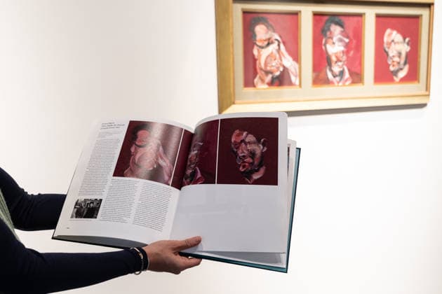 Sotheby s Icons and Bing Crosby Exhibitions press preview Member of personnel opens an exhibition companion book with reproduction of Francis Bacon Three Studies for Portrait of Lucian Freud in front of actual painting sold for almost 4 million dollars on view during press preview at Sotheby s Icons and Bing Crosby Exhibitions in New York, NY on December 13, 2025. New York New York United States Copyright: LevxRadin