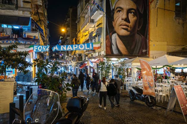 Via Forcella decorated for Christmas in the historic center of Naples, Italy. Naples, Italy - December 5, 2025: The characteristic Via Forcella in the historic center of the city, with Christmas decorations, the football team s banner, and the unmistakable mural by Jorit depicting San Gennaro. Naples NA Italy Copyright: xGennaroxLeonardix