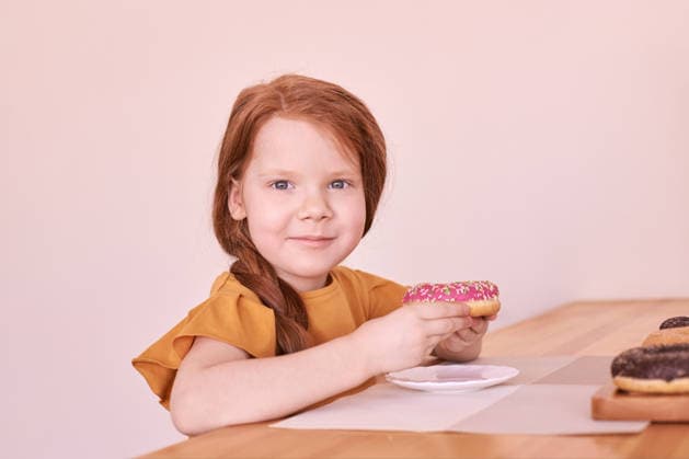 Kaukasisches weibliches Kind mit roten Haaren, das an einem Holztisch einen rosa Krapfen mit Zuckerguss genießt Caucasian female child with red hair enjoying a pink frosted doughnut at a wooden table. (License=RF) ,model released, Symbolfoto Copyright: xZoonar.com ElenaxSafonovax 24340207 ,model released, Symbolfoto ,property released