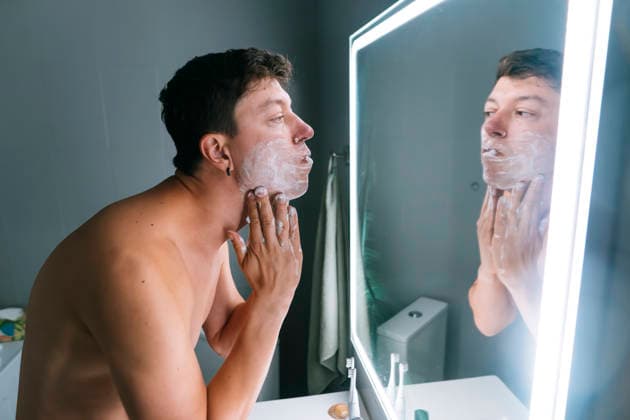 Rasieren am Morgen vor dem Vorstellungsgespräch - Mann bei der Körperpflege am LED-Spiegel shirtless man shaving at LED mirror in modern bathroom, applying foam and checking jawline, focused expression, sink with skincare (License=RF) ,model released, Symbolfoto Copyright: xZoonar.com OleksiixHrecheniukx 24345846 ,model released, Symbolfoto ,property released