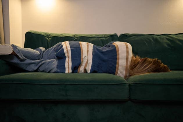 Gemütliche Einsamkeit mit einer auf dem Sofa ruhenden Frau bei sanftem Abendlicht Adult lies sideways on green couch wrapped in striped cardigan, dim wall lighting creating peaceful ambience, representing relaxation, comfort, and quiet personal space at end of digital day. (License=RF) ,model released, Symbolfoto Copyright: xZoonar.com SergeyxMironovx 24350038 ,model released, Symbolfoto ,property released