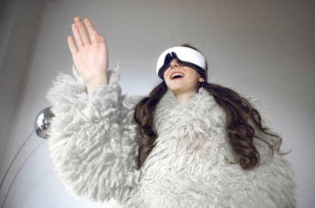 Eine junge Frau in einer gelben flauschigen Jacke und einer Virtual-Reality-Brille interagiert fröhlich mit der virtuellen Welt. Das lachende Mädchen mit langen Haaren gestikuliert und genießt den Prozess. A young woman in a yellow fluffy jacket and virtual reality glasses happily interacts with the virtual world. The laughing girl with long hair gestures and enjoys the process. Color of 2026 year, Cloud Dancer (License=RF) ,model released, Symbolfoto Copyright: xZoonar.com DashaxPetrenkox 24352321 ,model released, Symbolfoto ,property released