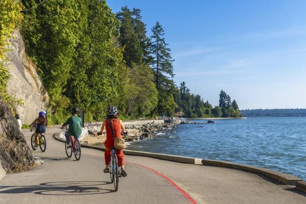 Touristen radeln auf der Ufermauer im Stanley Park und genießen an einem sonnigen Tag in Vancouver, Britisch Kolumbien, die malerische Aussicht auf das Meer und das Stadtbild Tourists are cycling on the seawall in stanley park, enjoying the scenic views of the ocean and cityscape on a sunny day in vancouver, british columbia Copyright: imageBROKER UnaixHuizi ibxuhu15971110.jpg ,model released, Symbolfoto ,property released
