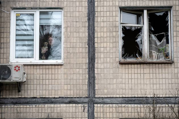 A woman holding a dog looks out of a surviving window in a five-storey residential building damaged by a Russian drone attack in the Sviatoshynskyi district of Kyiv, Ukraine, December 23, 2025. Falling Russian drone debris partially destroyed the roof and facade of the apartment block. Five people, including a child, were injured in the attack. (Photo by Danylo Antoniuk Ukrinform) Russian drone debris falls on apartment block in Kyiv  Copyright: xDanyloxAntoniukx
