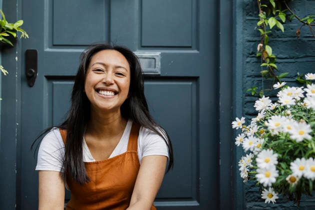Smiling woman sitting by entrance with flowers at home model released, Symbolfoto, ASGF06759