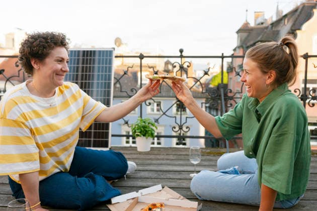 Smiling friends enjoying pizza on urban terrace with solar panel model released, Symbolfoto, FLMZF00915