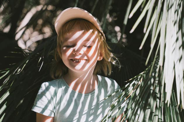 Playful child hiding behind palm leaves outdoors in sunlight model released, Symbolfoto, NDEF03045