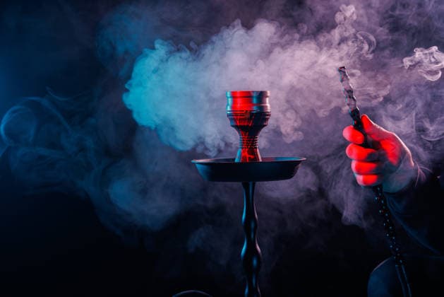 Hookah with smoke and colorful lighting, hand holding the mouthpiece in a dark atmosphere. Hookah with dense smoke and vibrant red-blue lighting, hand holding pipe hose in dark moody background., 96761246.jpg RECORD DATE NOT STATED