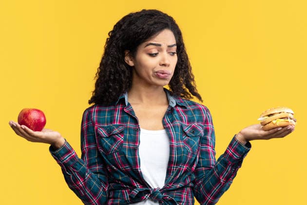 Hungry Black Woman Holding Burger And Apple Fruit Diet Concept. Unsure African American Woman Holding Burger And Apple Fruit. Hungry Lady Choosing Between Healthy And Unhealthy Food, Posing Isolated Over Orange Studio Background. Banner, model released, , 97053046.jpg RECORD DATE NOT STATED