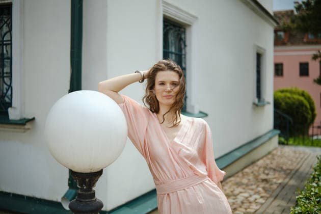 Woman posing by a light fixture near a white building in a sunny outdoor setting A woman poses confidently next to an street vintage light fixture, wearing a soft pink sundress. She stands against a charming white building, surrounded by greenery on a bright, sunny day., model released, , 97757740.jpg RECORD DATE NOT STATED
