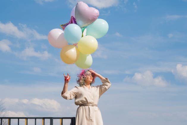 A woman with colored hair with an armful of balloons against a blue sky. A woman with colored hair with an armful of balloons against a blue sky, model released, , 97801082.jpg RECORD DATE NOT STATED
