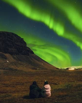 Romantisches Paar für zwei Personen, das unter lebendiger Aurora Borealis mit nördlicher Landschaft sitzt, magischer Winternachthimmel mit grünen Nordlichtern Two people romantic couple sitting under vivid aurora borealis with northern landscape, magical winter night sky with green northern lights Copyright: imageBROKER EvaldasxMikoliunas ibxemi15189371.jpg ,model released, Symbolfoto ,property released