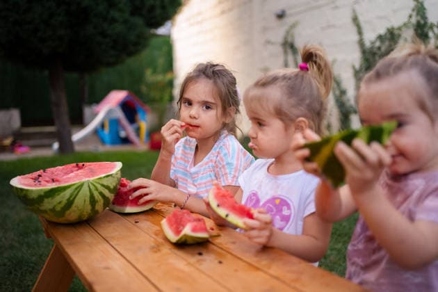 Joyful moments with friends enjoying fresh watermelon in the garden Three little girls savoring juicy watermelon slices together outside., model released, , 97919502.jpg RECORD DATE NOT STATED
