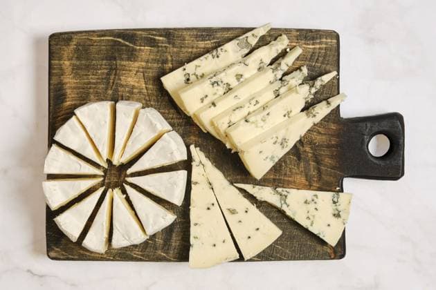 Verschiedene Käsesorten sind auf einem Holzbrett angeordnet. Ein Käse ist rund und in Spalten geschnitten. Ein anderer Typ wird in Dreiecke geschnitten. Die Platte zeigt eine Mischung aus Texturen und Formen Different types of cheese are arranged on a wooden board. One cheese is round and cut into wedges. Another type is sliced into triangles. The platter displays a mix of textures and shapes Copyright: imageBROKER AlekseixIsachenko ibxaii16111639.jpg