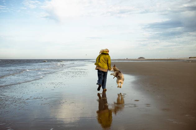 Woman running with dog on empty North Sea beach during joyful walk Sankt Peter-Ording, Schleswig-Holstein, Germany CR_PJJZ26010456-1916881-01 ,model released, Symbolfoto