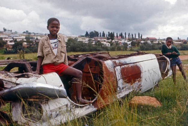 Zwei Kinder spielen an einem umgestürzten, verrosteten Autowrack auf einer offenen Grasfläche nahe einer Siedlung. Soweto, Südafrika, 10.08.1976. Johhanesburg Soweto Guateng Süd Afrika *** Two Children Play to a overturned, rusted Car Wreck at a open Grass area near a Settlement Soweto, South Africa, 10 08 1976 Johhanesburg Soweto Guateng South Africa Copyright: xUnitedxArchivesx xSvenxSimonxArchives SVS_94020000199