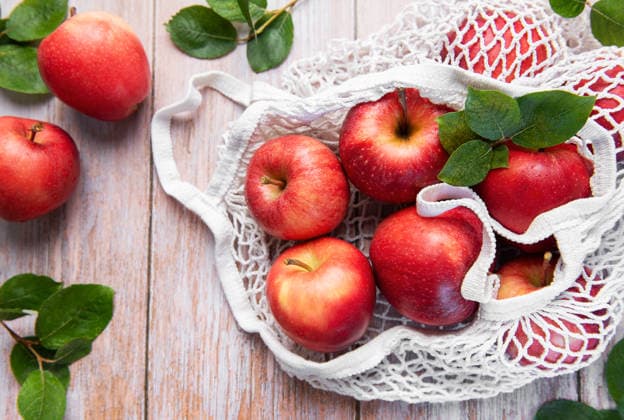 Ripe red apples with leaves are inside a reusable shopping bag on a wooden table, symbolizing a sustainable lifestyle Model Released OlenaRudo_ID32802_1116646_004 Copyright: xOlenaxRudox RECORD DATE NOT STATED