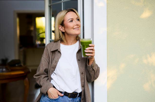 Smiling person with green smoothie standing on the patio at home model released, Symbolfoto property released, BSZF02945