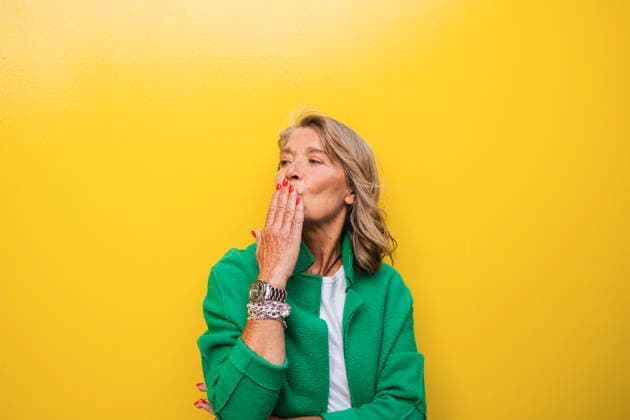 Mature woman blowing a kiss wearing green jacket on yellow background model released, Symbolfoto, JCCMF13811