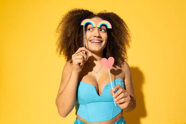 Smiling young woman with heart and rainbow prop posing against yellow background model released, Symbolfoto, MIKF00603