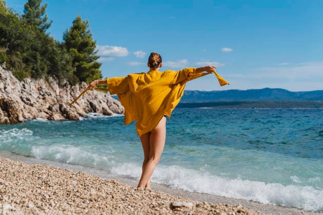 Woman in yellow cape enjoying playful moment by the sea on beach model released, Symbolfoto, NDEF03193