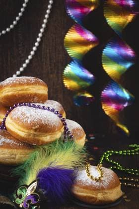 Berliner mit Puderzucker, geschmückt mit Perlenketten und bunten Spiralen vor einem dunklen Hintergrund, Fasching Berliner with powdered sugar, decorated with pearl necklaces and colorful spirals against a dark background, carnival Copyright: imageBROKER LucasxSeebacher ibxlse16280481.jpg