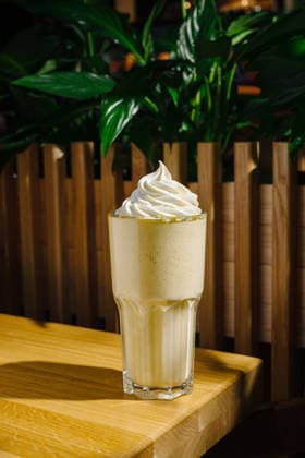 Köstlicher Milchshake mit Schlagsahne in einem gemütlichen Café A creamy milkshake with a generous swirl of whipped cream sits on a wooden table. Green plants in the background add a fresh touch, creating a warm cafe atmosphere. (License=RF) Copyright: xZoonar.com AntonxDobreax 24567797