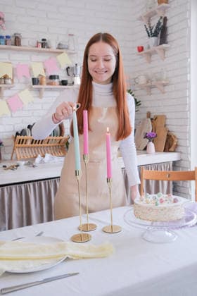 IMAGO Creative, Ostern, Bräuche, Osterbrunch Lächelnde Frau serviert das Osteressen und zündet Kerzen an. Caucasian woman serving table for Easter dinner, putting plates, cutlery, sweet cake and lighting candles (License=RF) ,model released, Symbolfoto Copyright: xZoonar.com IlonaxShorokhovax 24573771 ,model released, Symbolfoto ,property released