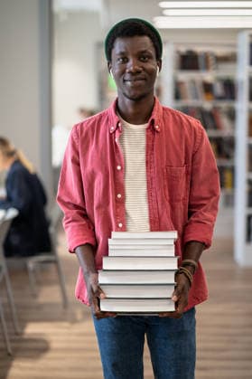 Porträt eines glücklichen afroamerikanischen Studenten mit einem Stapel Bücher in der Bibliothek Portrait of happy African American student guy holding pile of books smiling at camera while standing at library, enjoying studying and University life, selective focus. Education and self-study (License=RF) ,model released, Symbolfoto Copyright: xZoonar.com DmitriixMarchenkox xEnvatox 24579785 ,model released, Symbolfoto ,property released
