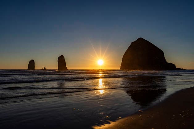 USA, Oregon, Sun setting behind haystack rock on Cannon Beach , 31.07.2024, ,property released TTBB_tbs5133180.jpg, Horizontal,Pacific Ocean,Oregon Coast,Empty,Outdoors,Haystack Rock,Sunset,Rock Formation,No People,Landscape - Scenery,Scenics - Nature,Tranquil Scene,Travel,Sea,Coastline,Beach,Sand,Surf,Sun,Sunlight,Clear Sky,Horizon Over Water,Reflection,Cannon Beach,Landscape,Water s Edge,In Silhouette,Copy Space,Oregon,USA Copyright: xTetraxImages StevexSmithx