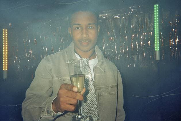 Junger Mann hält ein Glas mit einem prickelnden Getränk in der Hand und feiert während einer festlichen Veranstaltung in einem Club mit Partydekorationen und Neonlichtern und sorgt so für eine lustige Atmosphäre Young man holding a glass with a sparkling drink, celebrating during a festive event in a club with party decorations and neon lights, creating a fun atmosphere Copyright: imageBROKER UnaixHuizi ibluhu16502972.jpg ,model released, Symbolfoto ,property released
