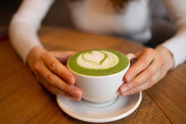 Feminine Hände halten Keramikbecher mit Matcha Latte, zarte herzförmige Schaummuster sichtbar, hölzerne Oberfläche Hintergrund schaffen gemütliche Kaffee Moment Woman s hands cradling a cup of matcha latte, featuring a heart-shaped design in the creamy foam, resting on a wooden table while savoring a warm, comforting beverage (License=RF) ,model released, Symbolfoto Copyright: xZoonar.com ElenaxShishkinax 23243727 ,model released, Symbolfoto ,property released
