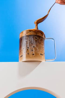 IMAGO Creative, Food, Trend, Iced Coffee Milky coffee action shot with spoon and glass mug An action shot capturing a creamy affogato pouring into a clear glass mug, with swirls of milk blending into rich coffee against a vibrant blue background. Model Released CintiaViudez_ID32864_1119261_002 Copyright: xCintiaxViudezx RECORD DATE NOT STATED